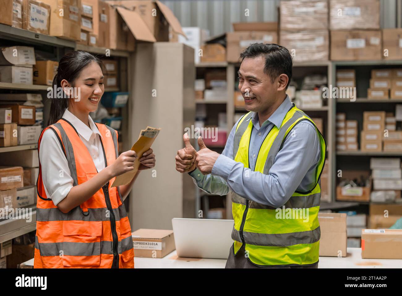 Young warehouse woman worker happy with salary cash bonus money admire thumbs up from manager for good working Stock Photo