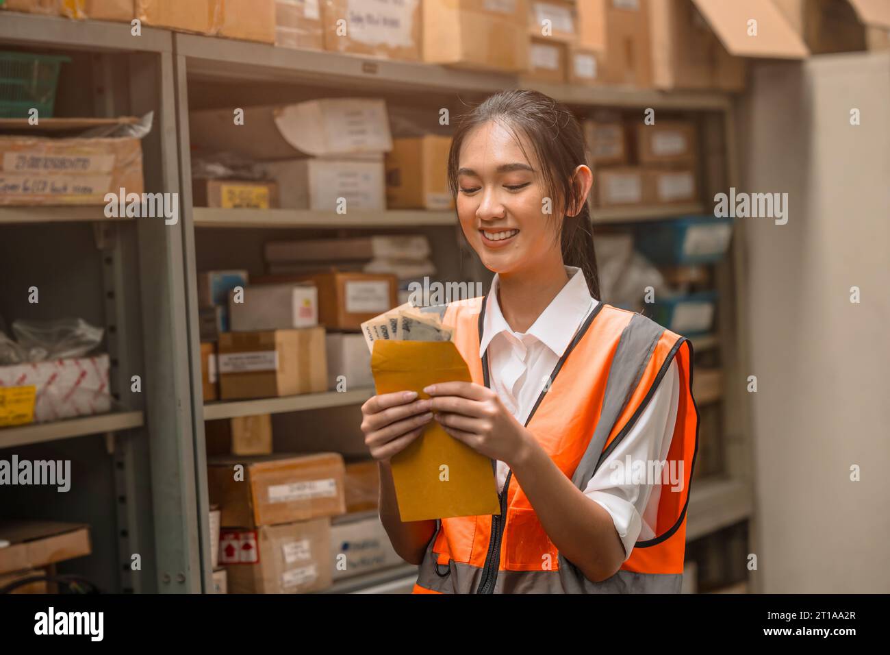 Young warehouse woman worker happy with salary cash bonus money from hard working in inventory industry Stock Photo