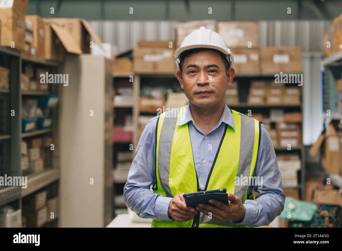Portrait senior engineer happy working inventory manager. Southeast Asian adult male worker standing in factory store warehouse. Stock Photo