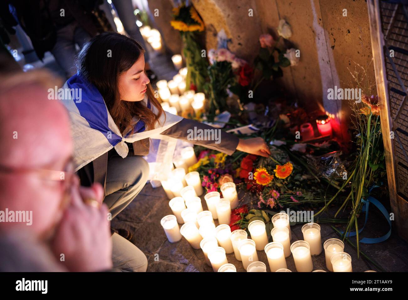 Munich, Germany. 12th Oct, 2023. A young woman wrapped in an Israel flag lays flowers in front of Munich's main synagogue Ohel Jakob during a memorial service organized by the Jewish Community of Munich and Upper Bavaria. The commemoration was held under the motto 'Mourning alongside Israel'. Credit: Matthias Balk/dpa/Alamy Live News Stock Photo