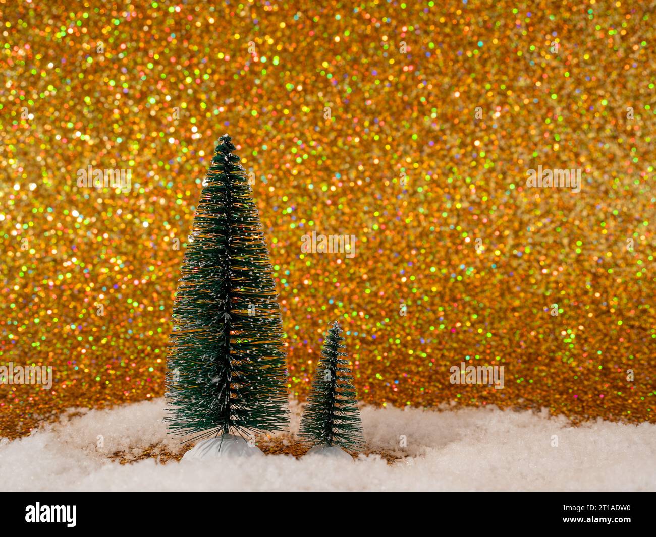 The photo shows a festive scene with decorative artificial Christmas trees set on shiny white snow. The backdrop features a shimmering gold backdrop t Stock Photo