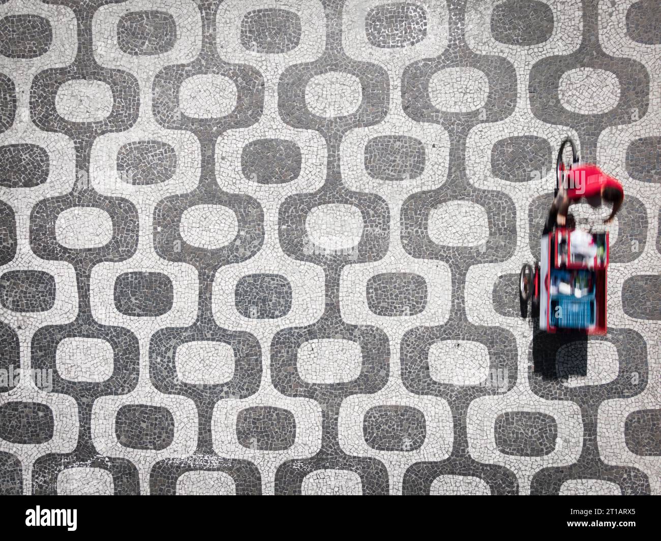 Top down aerial view showing a street vendor cycling on the iconic Ipanema Beach mosaic sidewalk in Rio de Janeiro, Brazil. Stock Photo