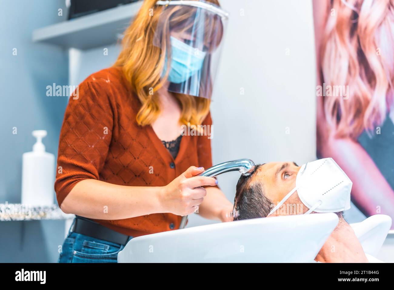 Reopening of hairdressing salons after the Coronavirus pandemic. Hairdresser with face mask and protective screen, covid-19. Social distance, new Stock Photo