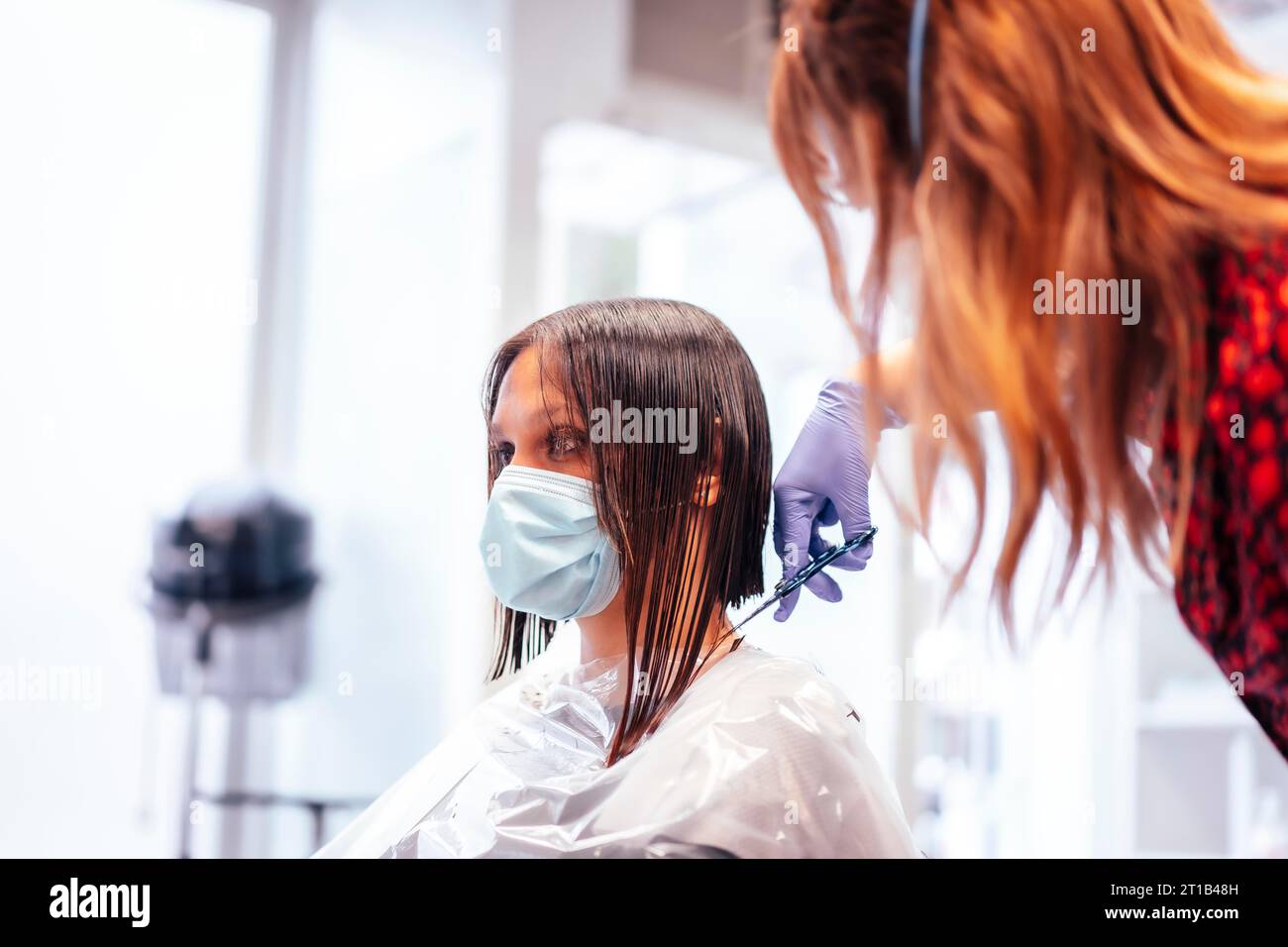 Hairdresser with mask and gloves cutting the ends of the hair to the