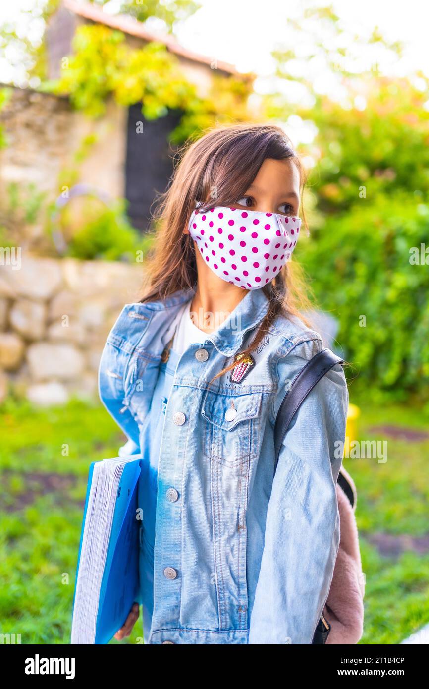 Caucasian girl with face mask ready to go back to school. New normality, social distance, coronavirus pandemic, covid-19. Jacket, backpack and a blue Stock Photo