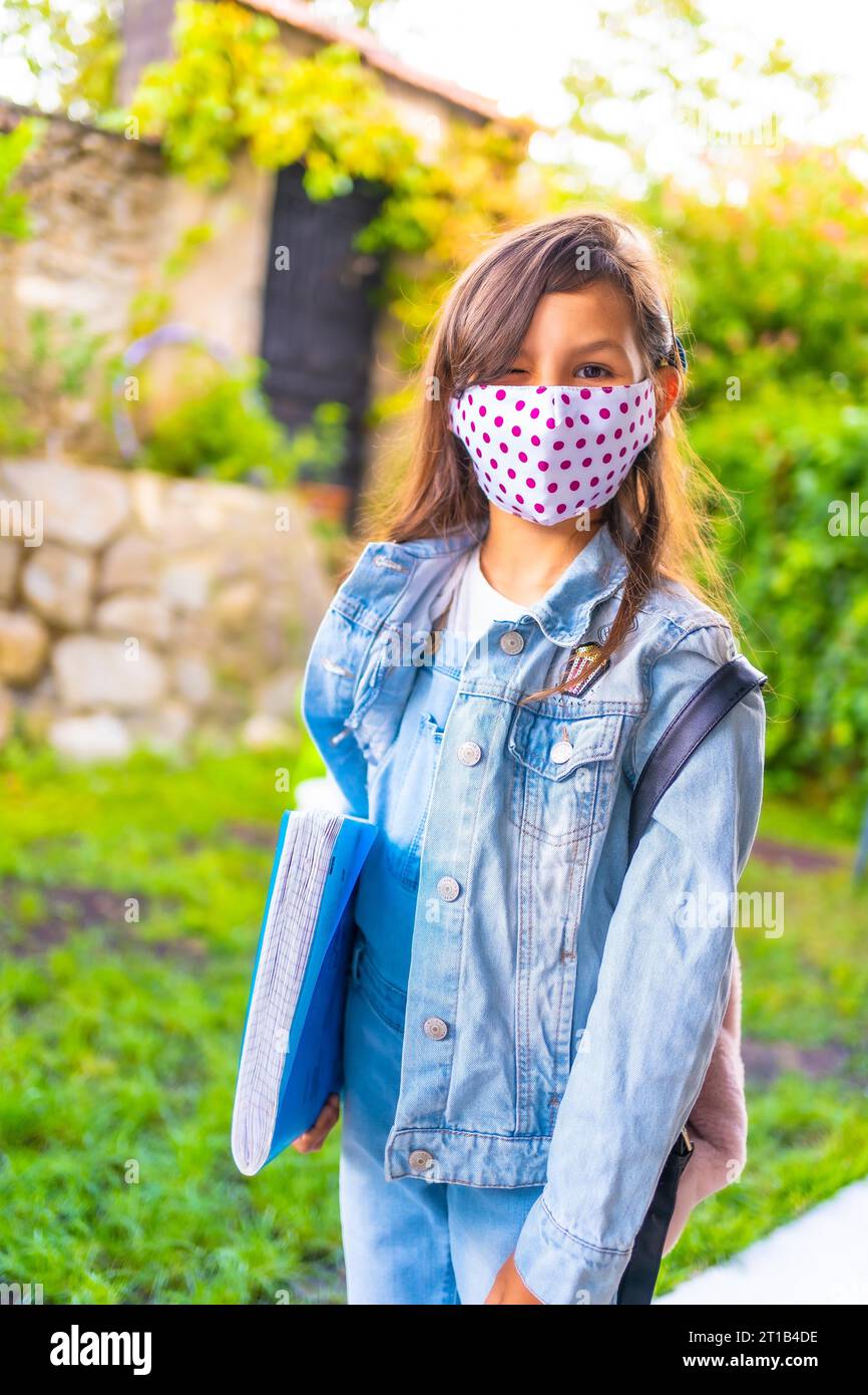 Caucasian girl with face mask ready to go back to school. New normality, social distance, coronavirus pandemic, covid-19. Jacket, backpack and a blue Stock Photo