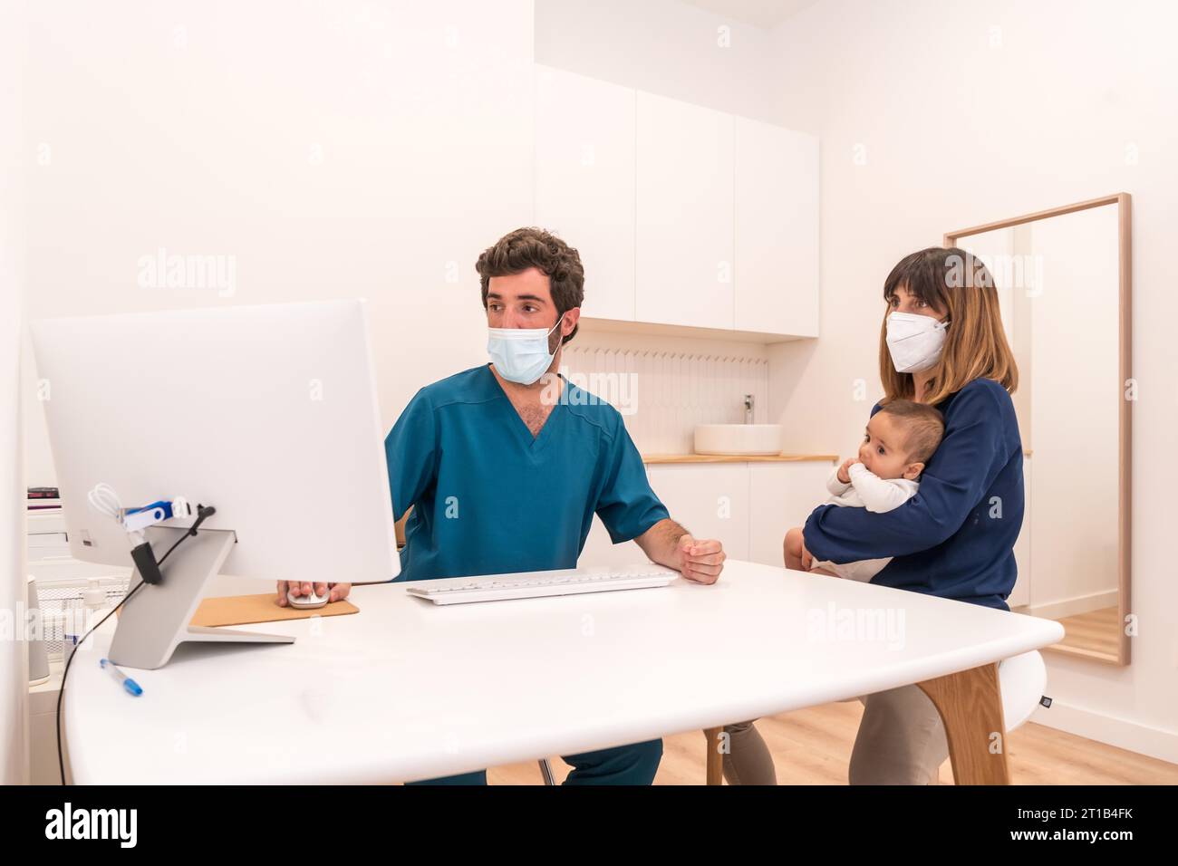 Doctor using a computer to show the medical report to a mother with baby in arms in a hospital Stock Photo