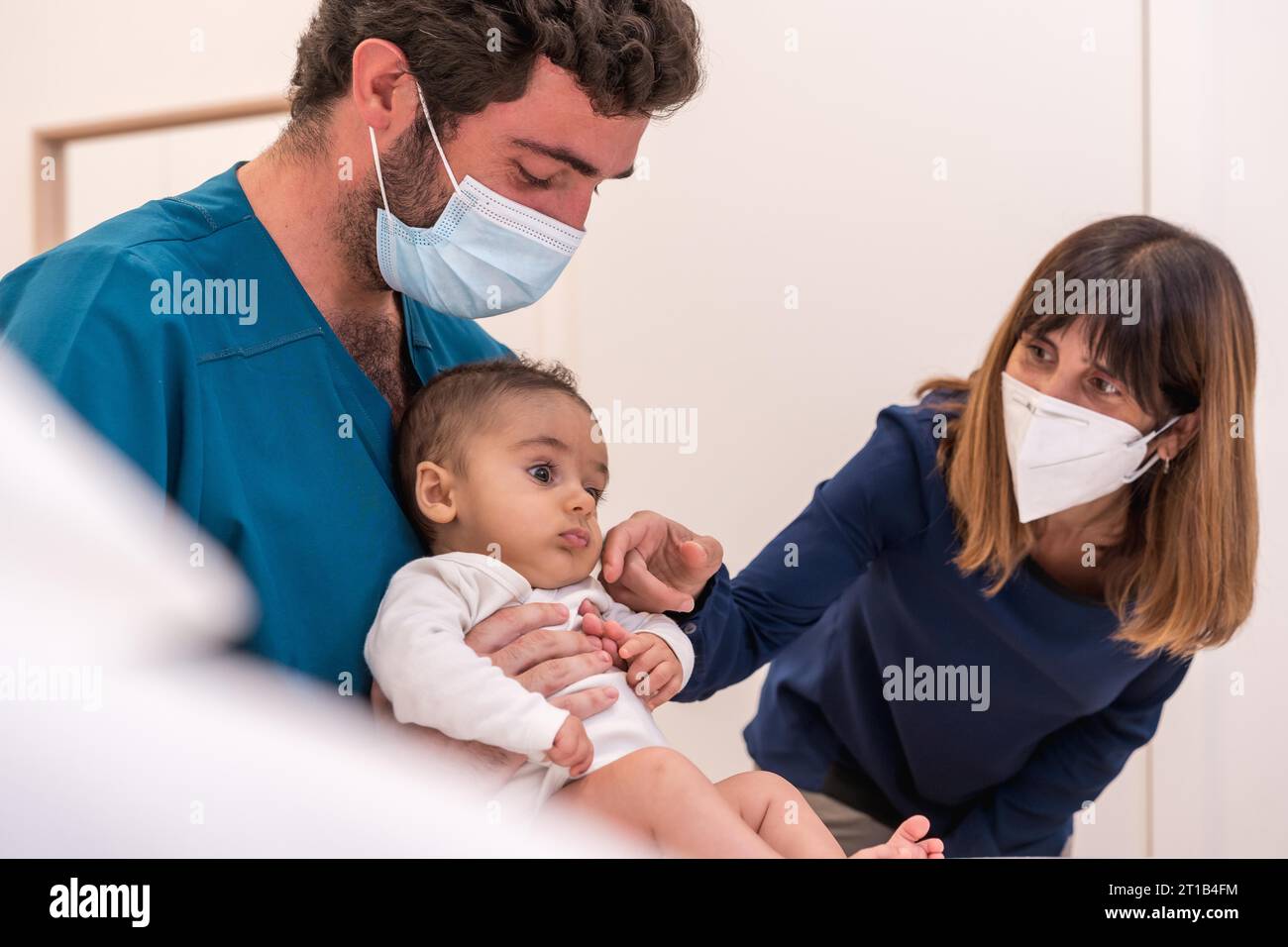 Doctor holding a baby next to his mother during a medical exam Stock Photo