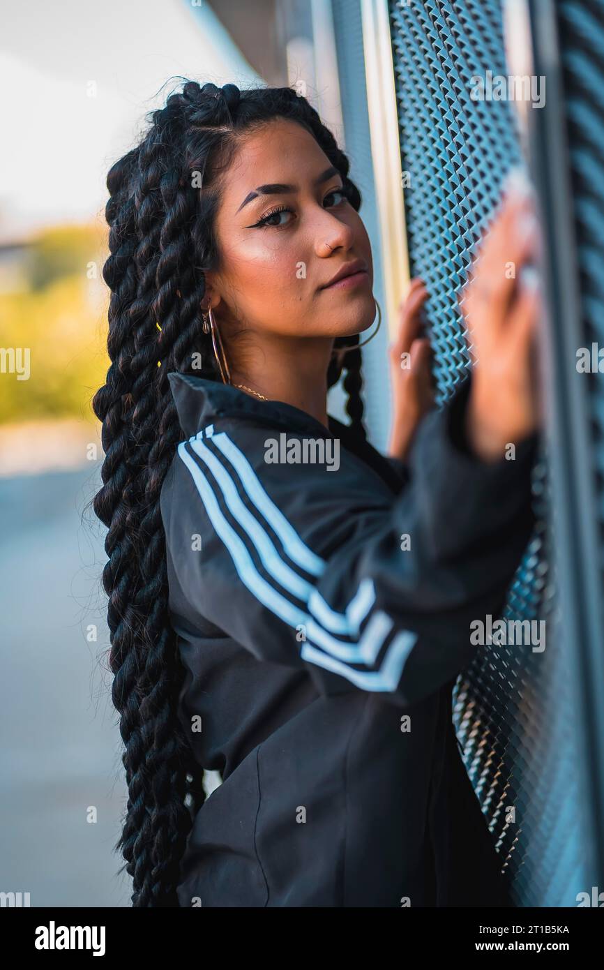 Urban session. Young black ethnic woman with long braids and with tattoos, looking glass, smiling Stock Photo