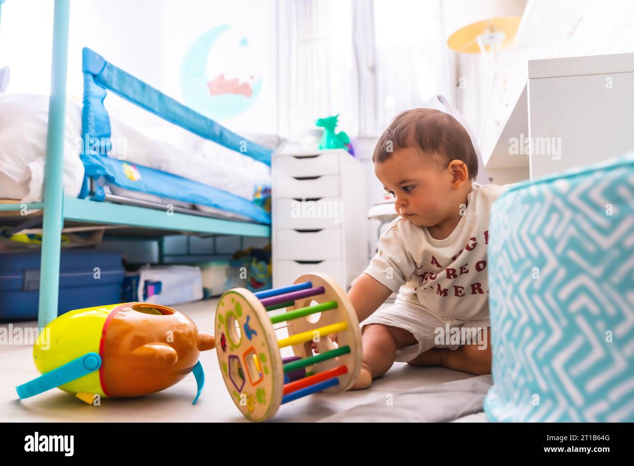 Young Caucasian mother playing with her in the room with toys. Baby less than a year learning the first lessons of her mother. Boy playing on the Stock Photo