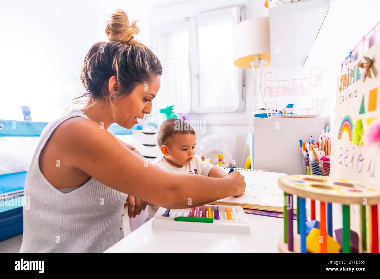 Young Caucasian mother playing with her in the room with toys. Baby less than a year learning the first lessons of her mother. Painting with color Stock Photo