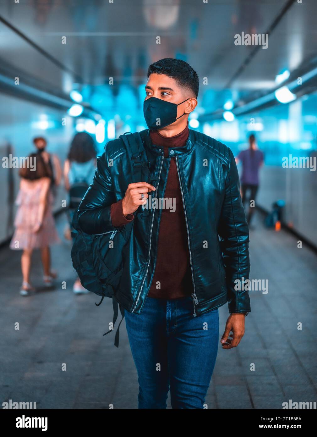 Fashion lifestyle, portrait of a young Latino in the city subway. Jeans, leather jacket and brown shoes. In a pandemic with a mask Stock Photo