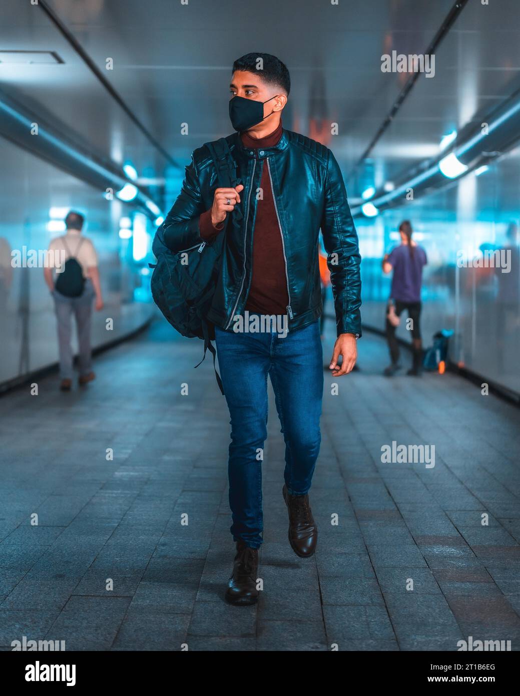Fashion lifestyle, portrait of a young Latino in the city subway. Jeans, leather jacket and brown shoes. In a pandemic with a mask Stock Photo