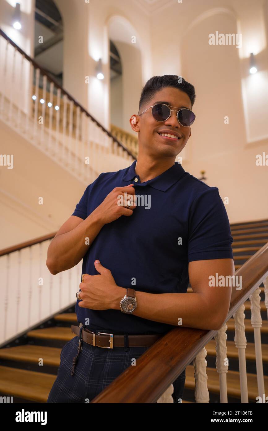 Fashion lifestyle, portrait of a young Latino man in a beautiful old building. Blue polo shirt and plaid pants. Portrait by the stairs Stock Photo