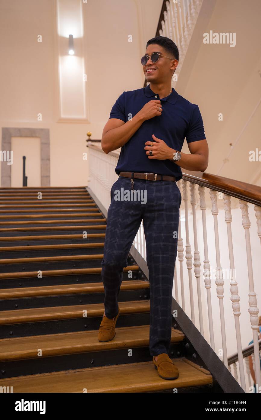 Fashion lifestyle, portrait of a young Latino man in a beautiful old building. Blue polo shirt and plaid pants. Portrait by the stairs Stock Photo