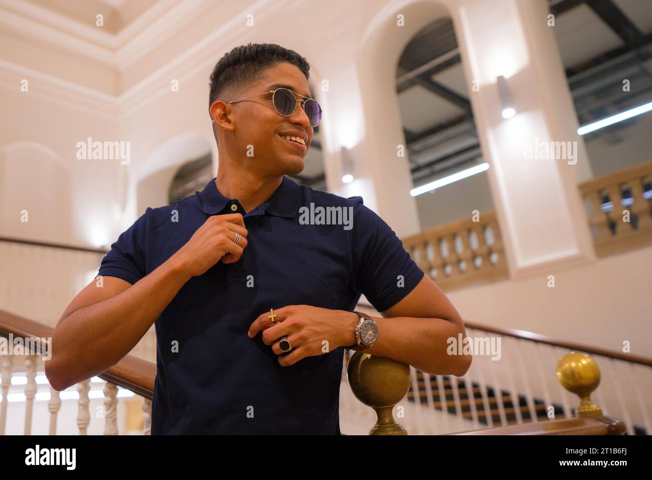 Fashion lifestyle, portrait of a young Latino man in a beautiful old building. Blue polo shirt and plaid pants. Portrait by the stairs Stock Photo