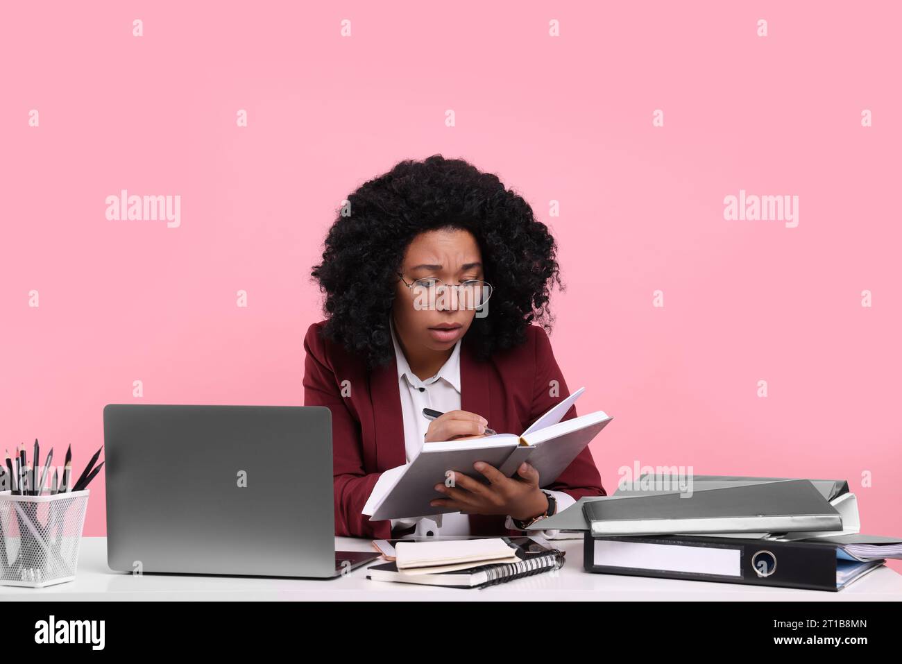 Stressful deadline. Tired woman working at white desk against pink background Stock Photo