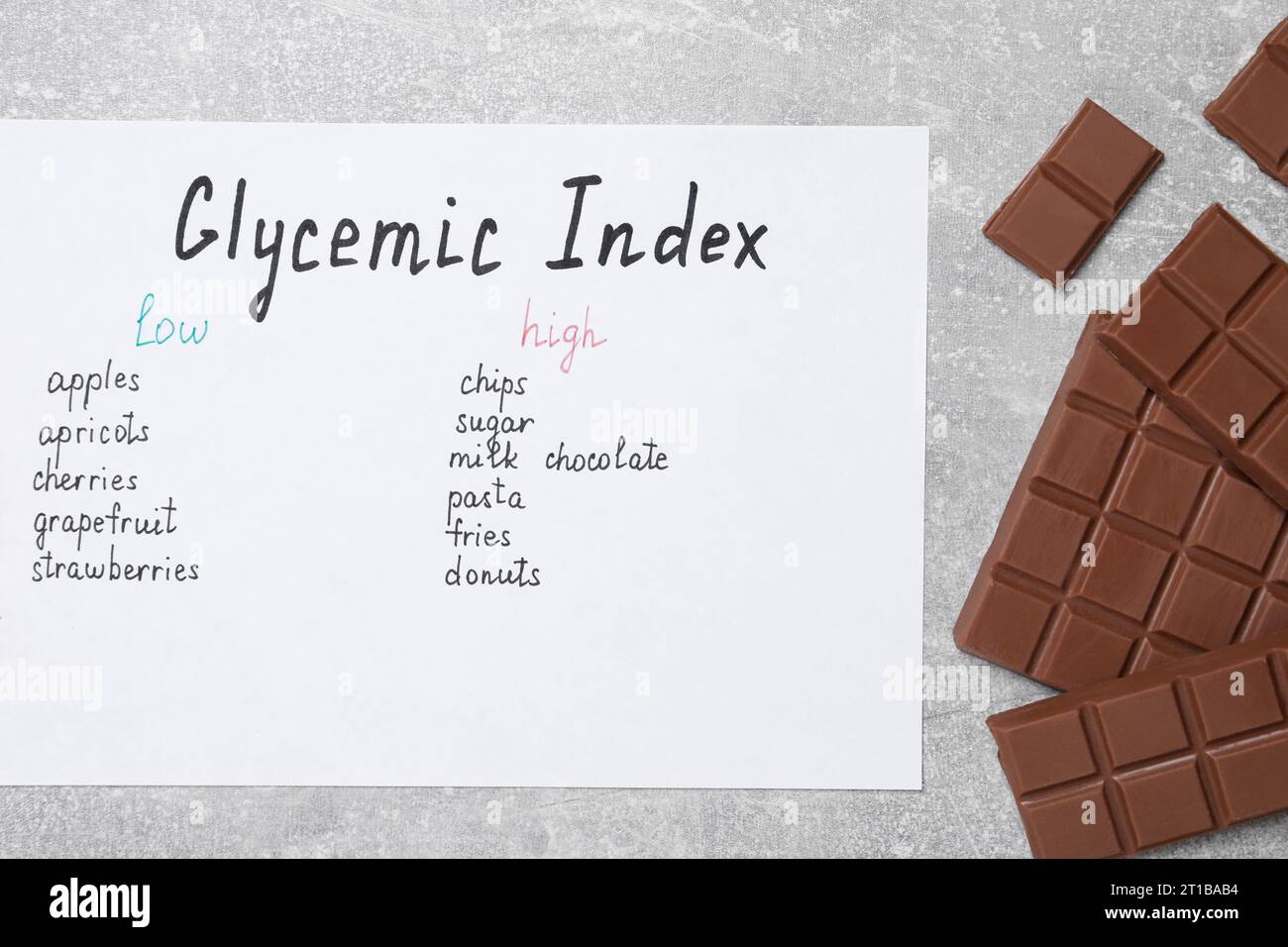 List with products of low and high glycemic index and chocolate on light grey table, top view Stock Photo