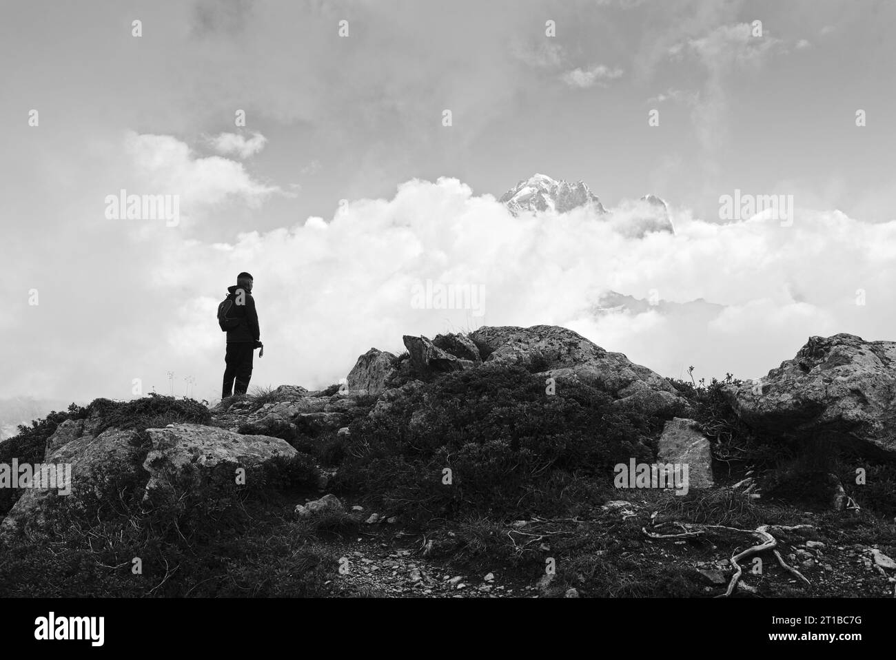 Young man at the top of a mountain admiring a peak in the middle of a cloudy sky Stock Photo