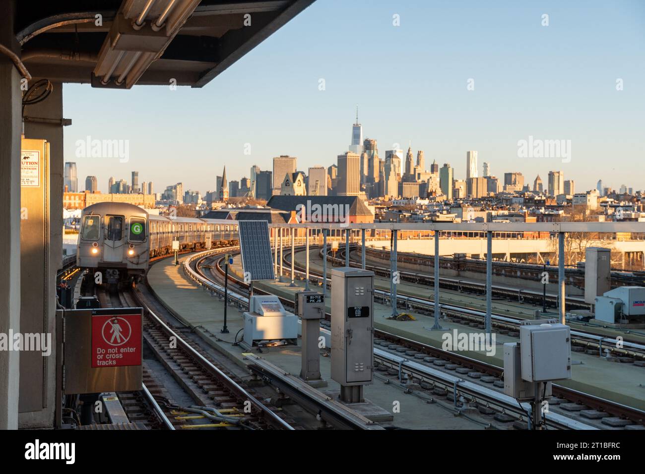Golden hour view of New York City skyline and an approaching G train at Sunrise on the elevated railroad portion of the G line at Smith Street. Stock Photo