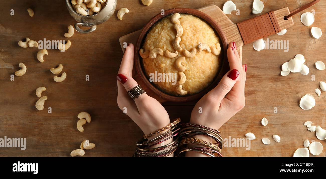 Female hands and plate with traditional Indian food pongal on wooden table, top view Stock Photo