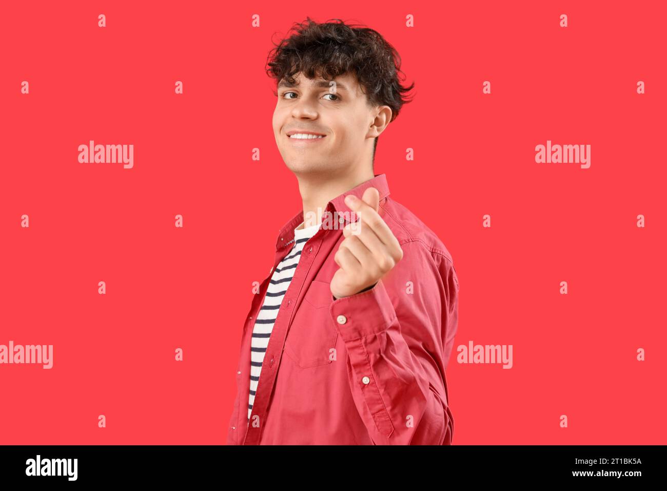 Handsome young man making heart with his fingers on red background ...