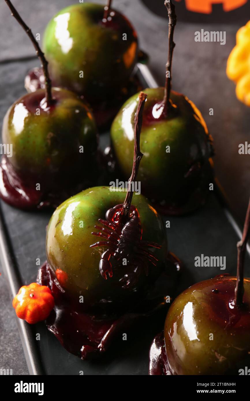 Board of tasty caramel apples for Halloween and scorpion on black background Stock Photo