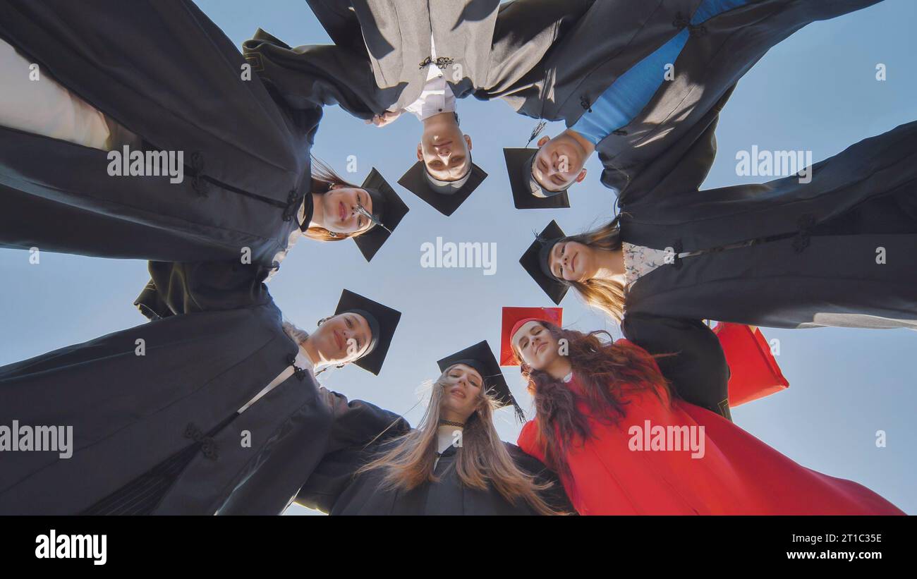 College graduates in a circle stand hugging each other. Stock Photo