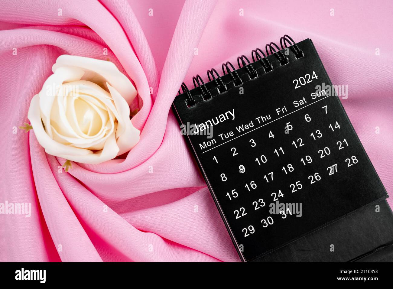 January 2024 desk calendar black color and rose on pink textile ...