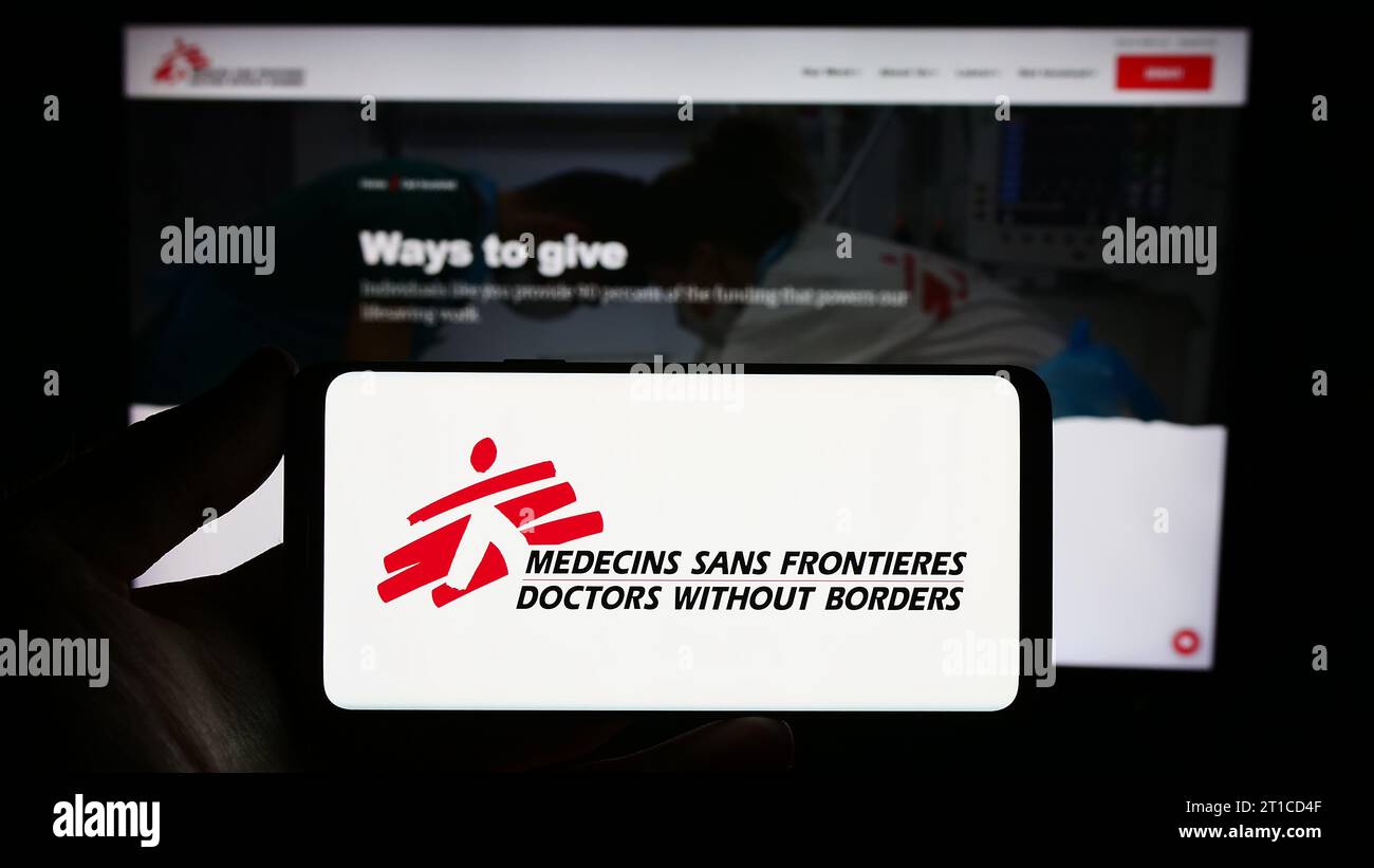 Person holding smartphone with logo of charity organization Doctors Without Borders in front of website. Focus on phone display. Stock Photo