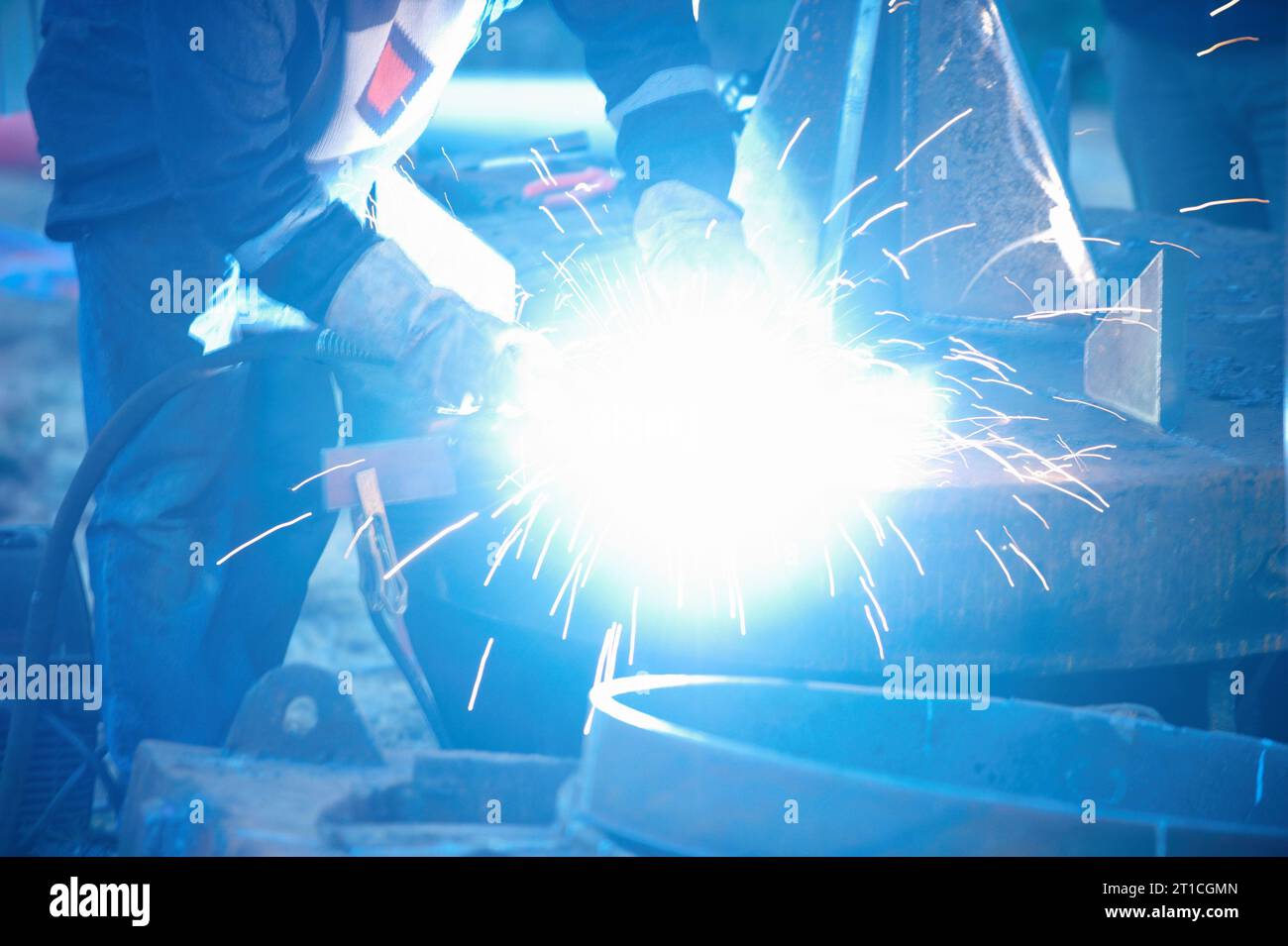 Industrial electrode welder with face shield and blue overall welding a