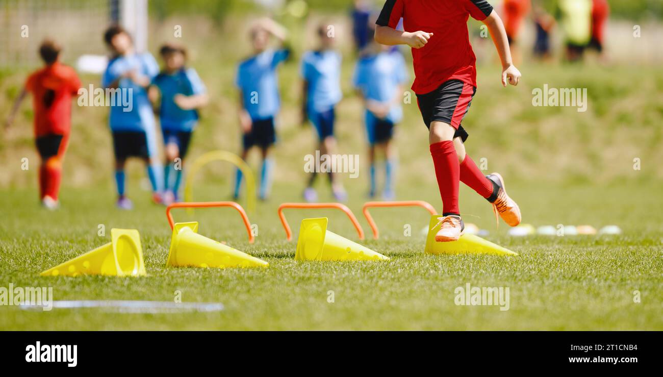 Happy children jumping over sports hurdles on the training pitch. Group of school kids attending sports agility training on a sunny summer day. Soccer Stock Photo