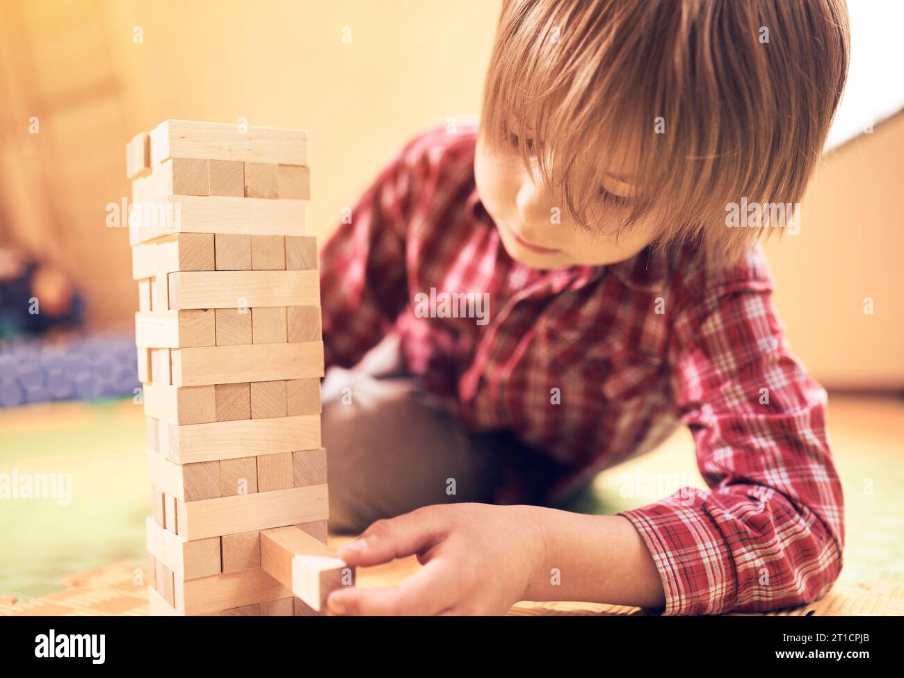 Preschool cute boy playing in a table game with wooden blocks at home