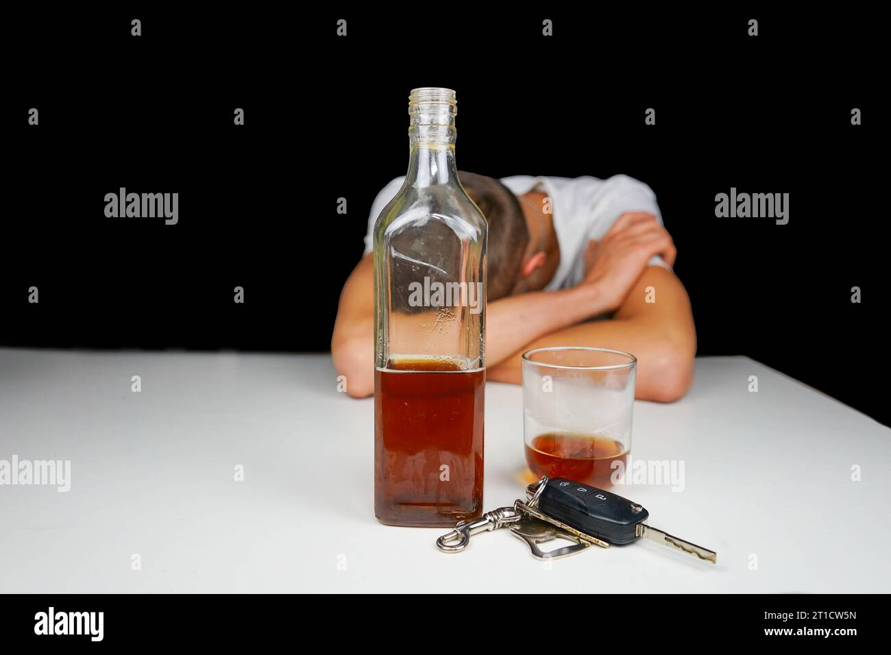 Car keys and alcohol on the table. Drunk man sleeping on the table with bottle of whiskey and drink. Alcoholism. Don't drive when you're drunk. Stock Photo