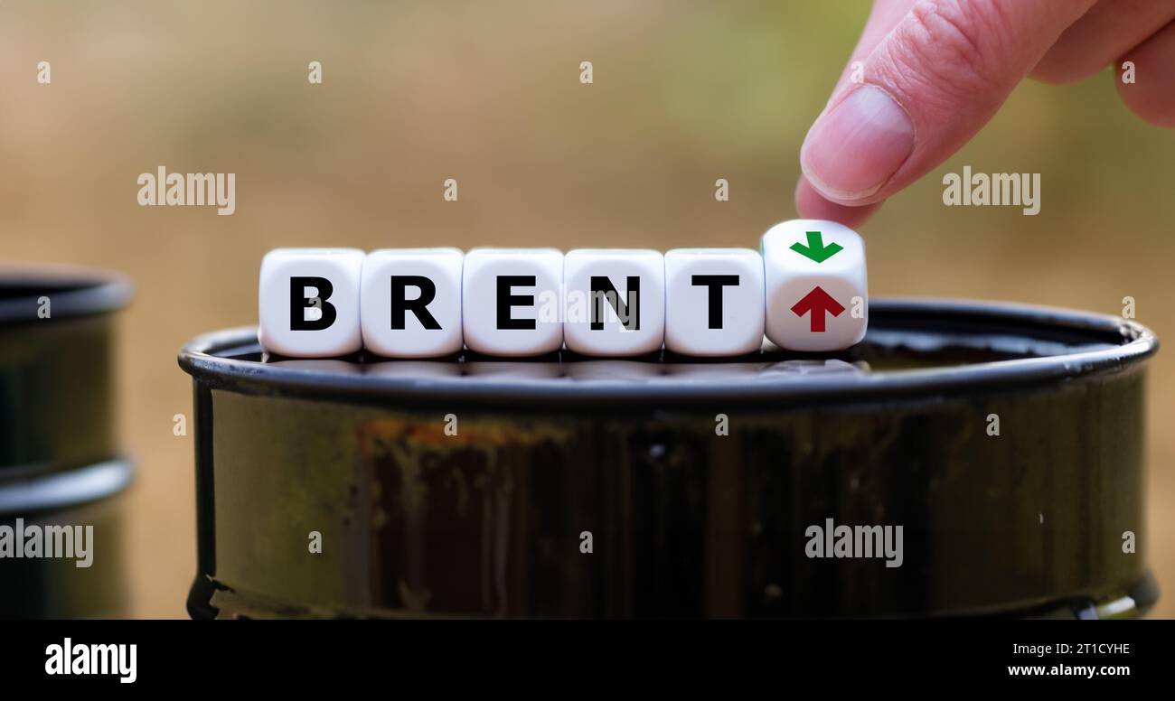 Hand turns dice and changes the up and down arrow next to the word Brent. Symbol for an increasing or decreasing oil price. Stock Photo