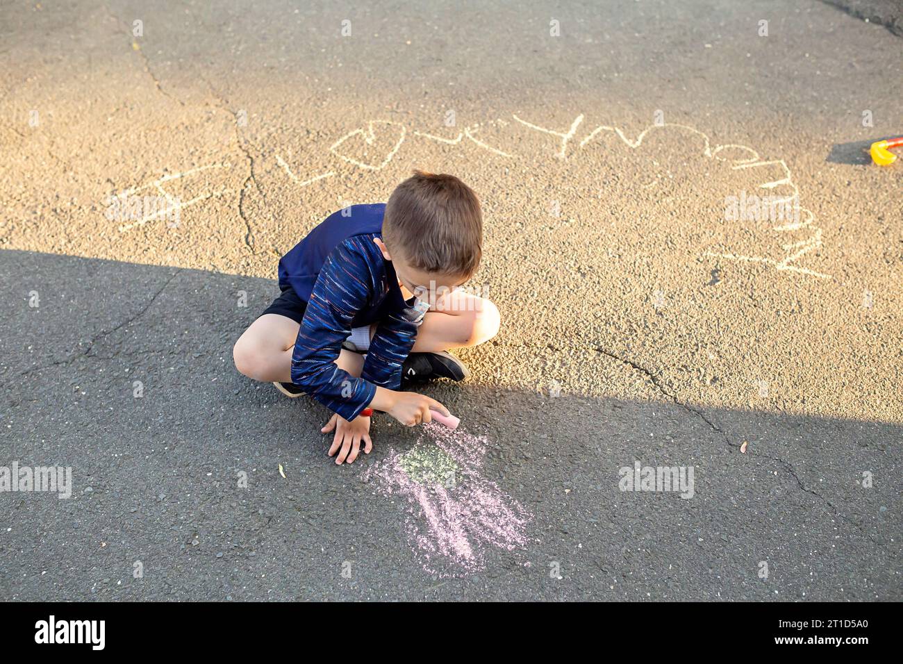 Young boy drawing on the driveway with chalk Stock Photo - Alamy