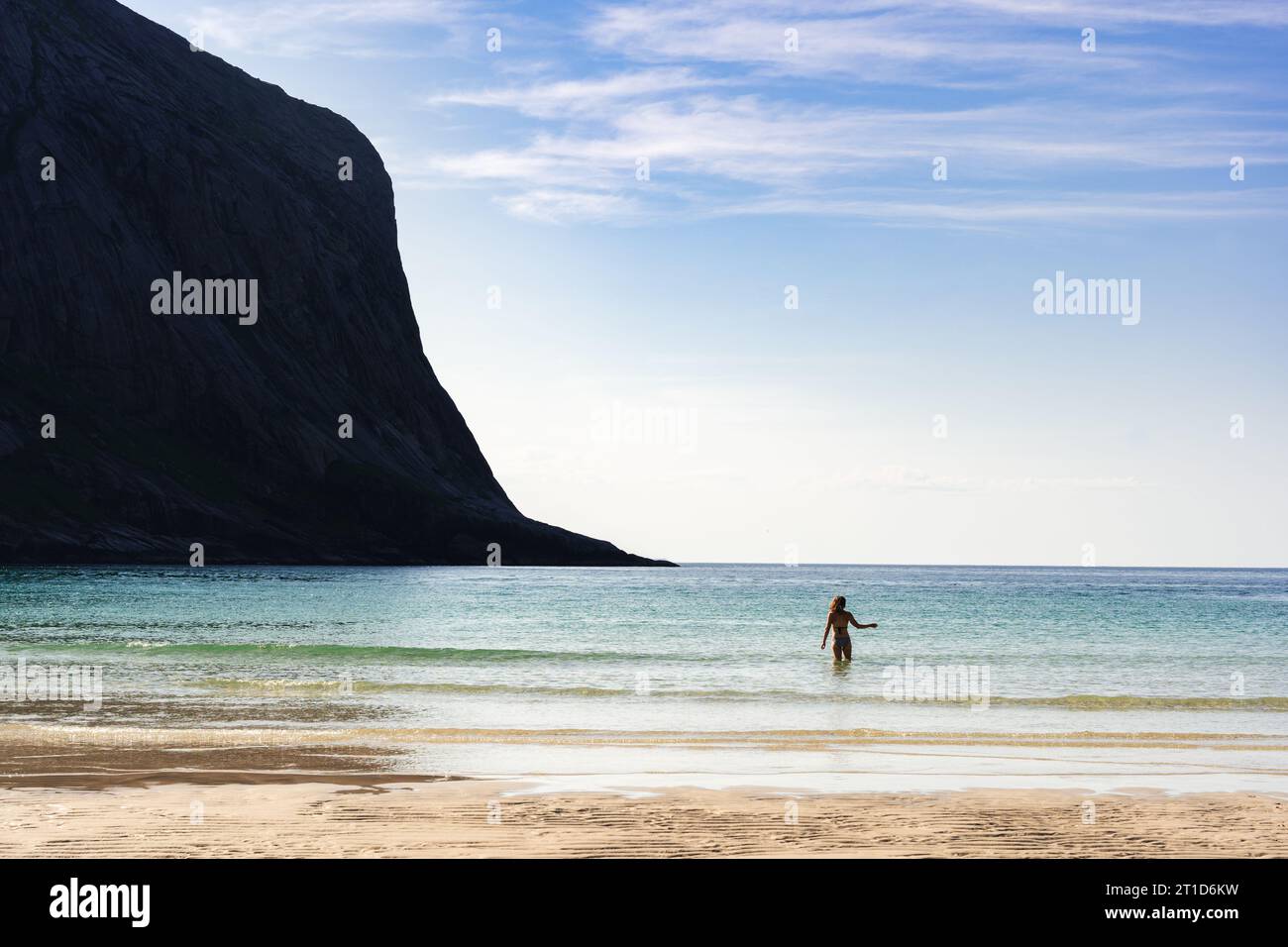 Woman in ocean water under large cliff Stock Photo
