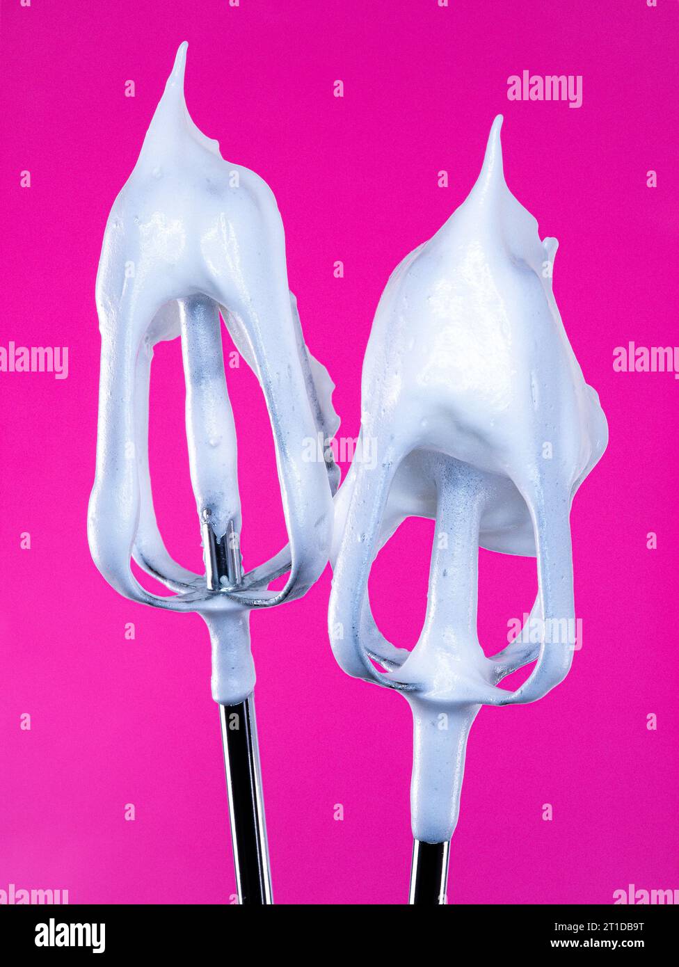 A pair of electric whisk beaters smothered in a luxuriously soft glossy white meringue mixture, pictured against a bold and vibrant backdrop. Stock Photo