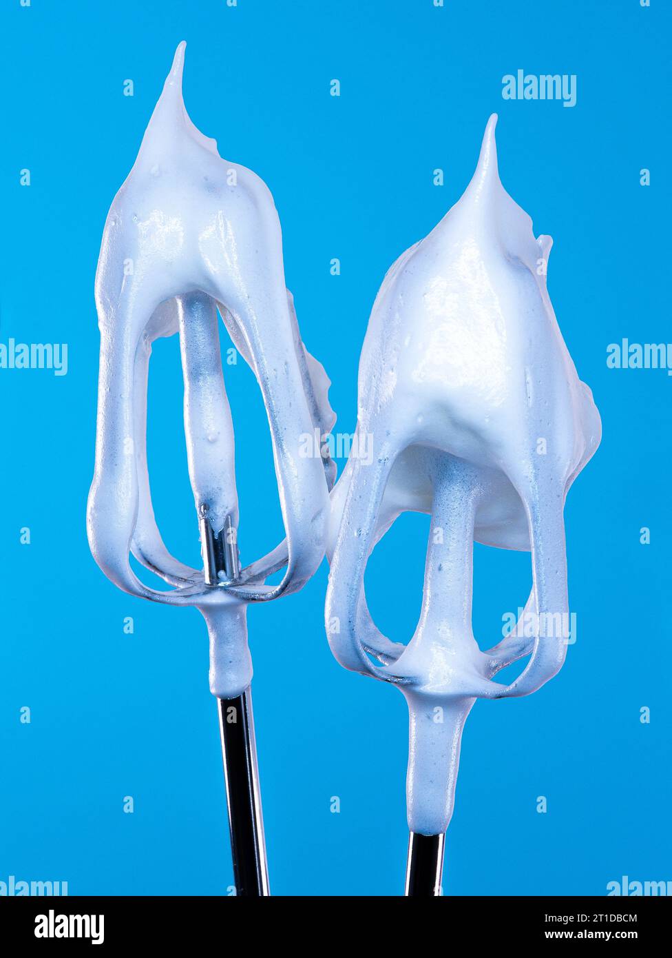 A pair of electric whisk beaters smothered in a luxuriously soft glossy white meringue mixture, pictured against a bold and vibrant backdrop. Stock Photo