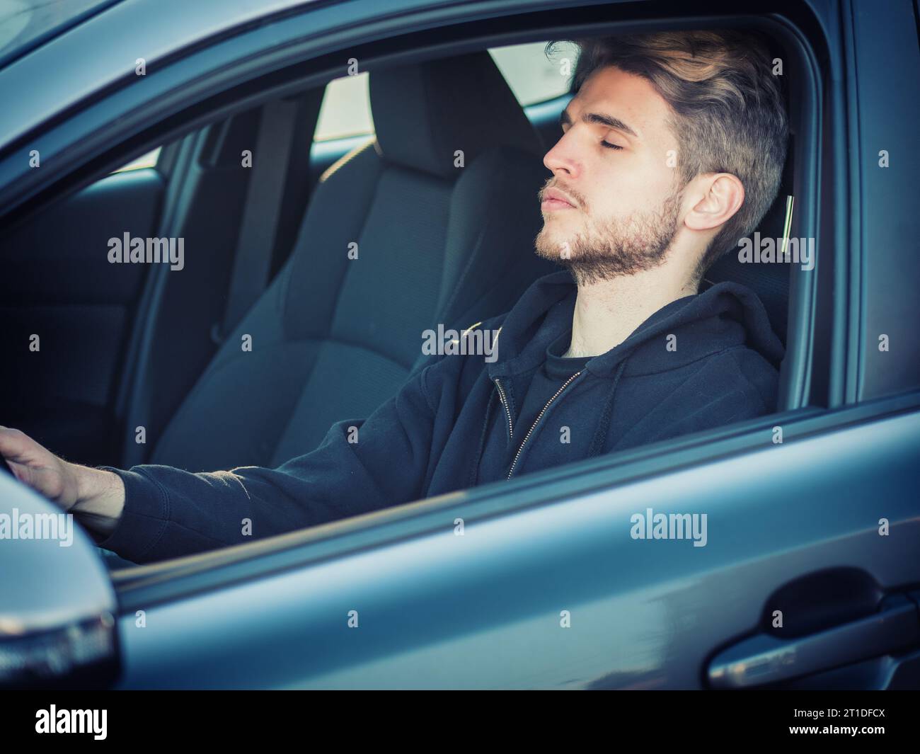 A man sitting in a car with his eyes closed sleeping or falling asleep