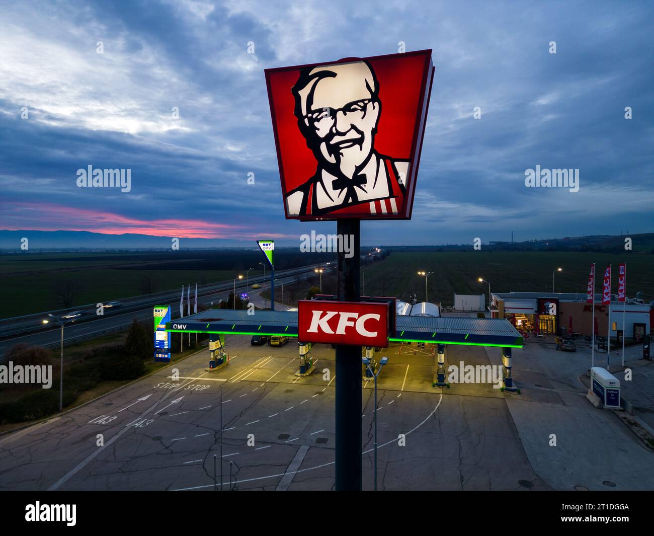Belozyom, Bulgaria - december 24, 2022 KFC fast food restaurant sign at OMV gas station on a highway in the evening aerial view. Stock Photo
