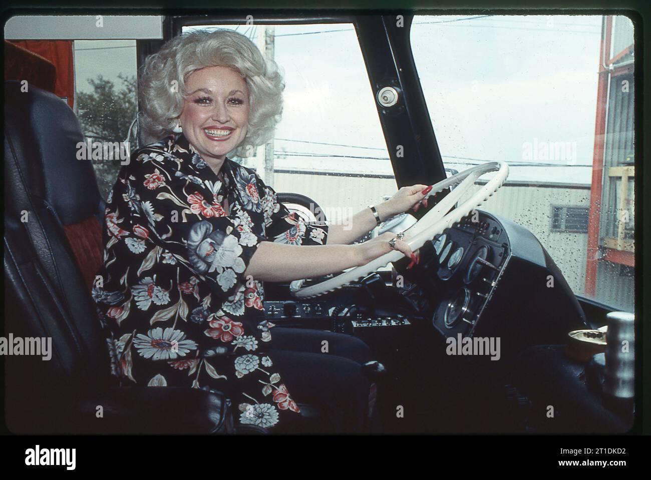 A photo of the great Dolly Parton posing behind the wheel on her tour