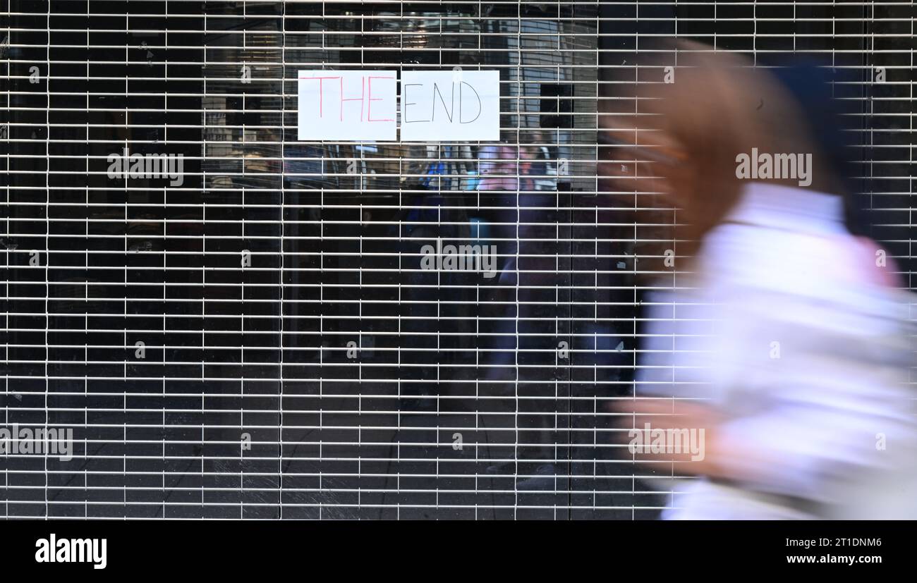 Stuttgart, Germany. 13th Oct, 2023. A passerby walks past a closed shopping store in the city center, on which a sign with the inscription: "The End" hangs on the lowered roller shutter (wiping effect due to long exposure). (to dpa "More company bankruptcies in Germany") Credit: Bernd Weißbrod/dpa/Alamy Live News Stock Photo