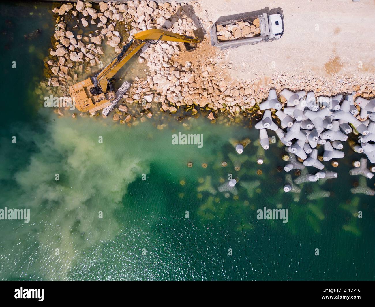 An excavator diligently constructs a dock or breakwater in the sea, its ...