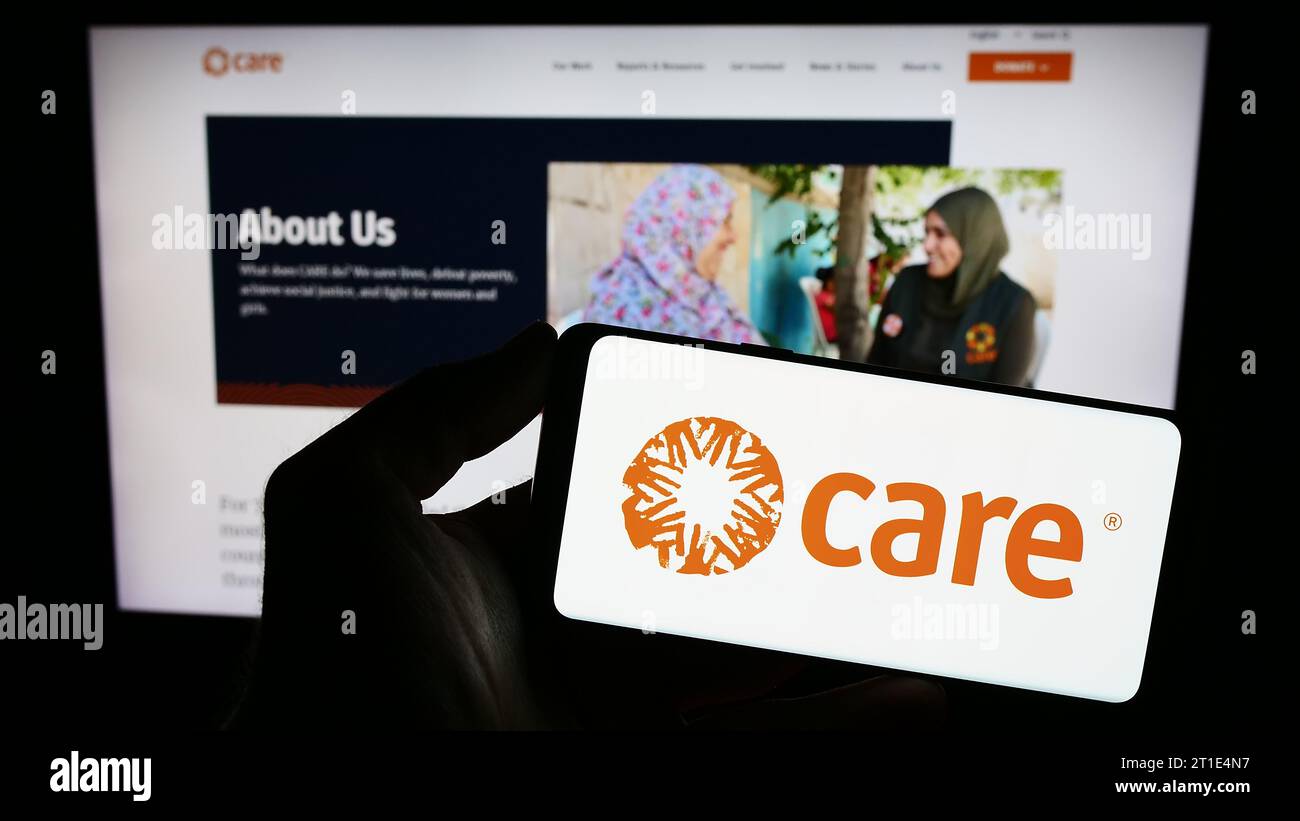 Person holding smartphone with logo of humanitarian agency CARE International in front of website. Focus on phone display. Stock Photo