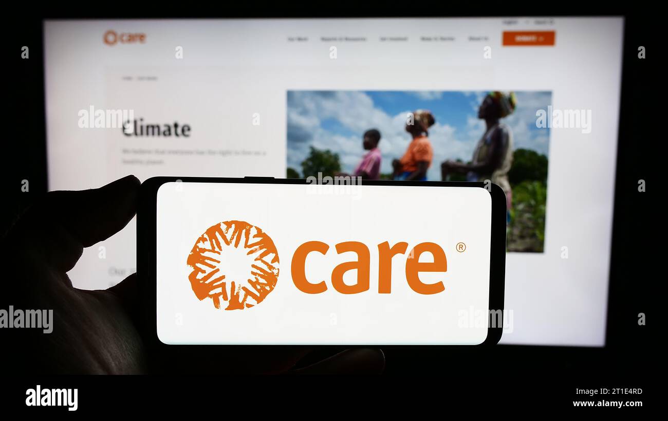 Person holding cellphone with logo of humanitarian agency CARE International in front of webpage. Focus on phone display. Stock Photo