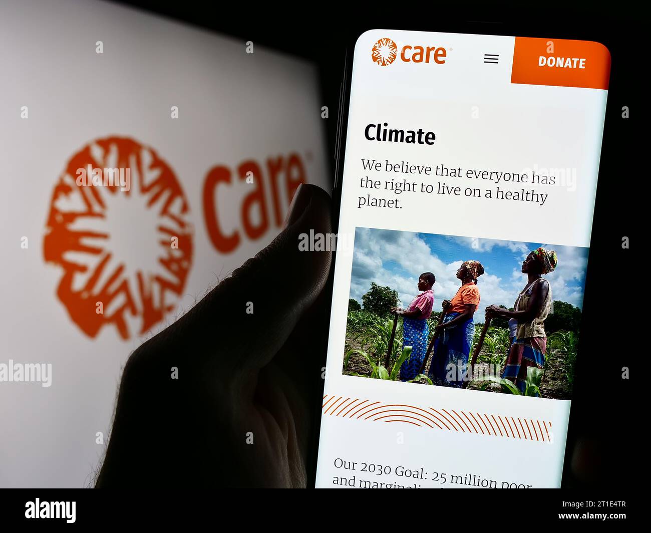 Person holding cellphone with webpage of humanitarian agency CARE International in front of logo. Focus on center of phone display. Stock Photo