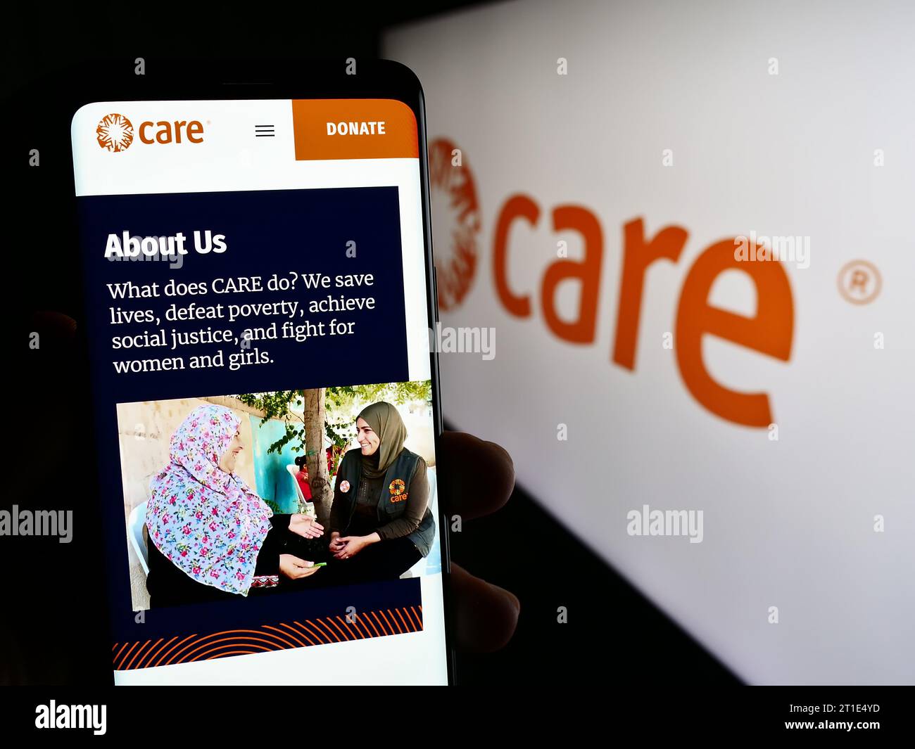 Person holding smartphone with web page of humanitarian agency CARE International in front of logo. Focus on center of phone display. Stock Photo