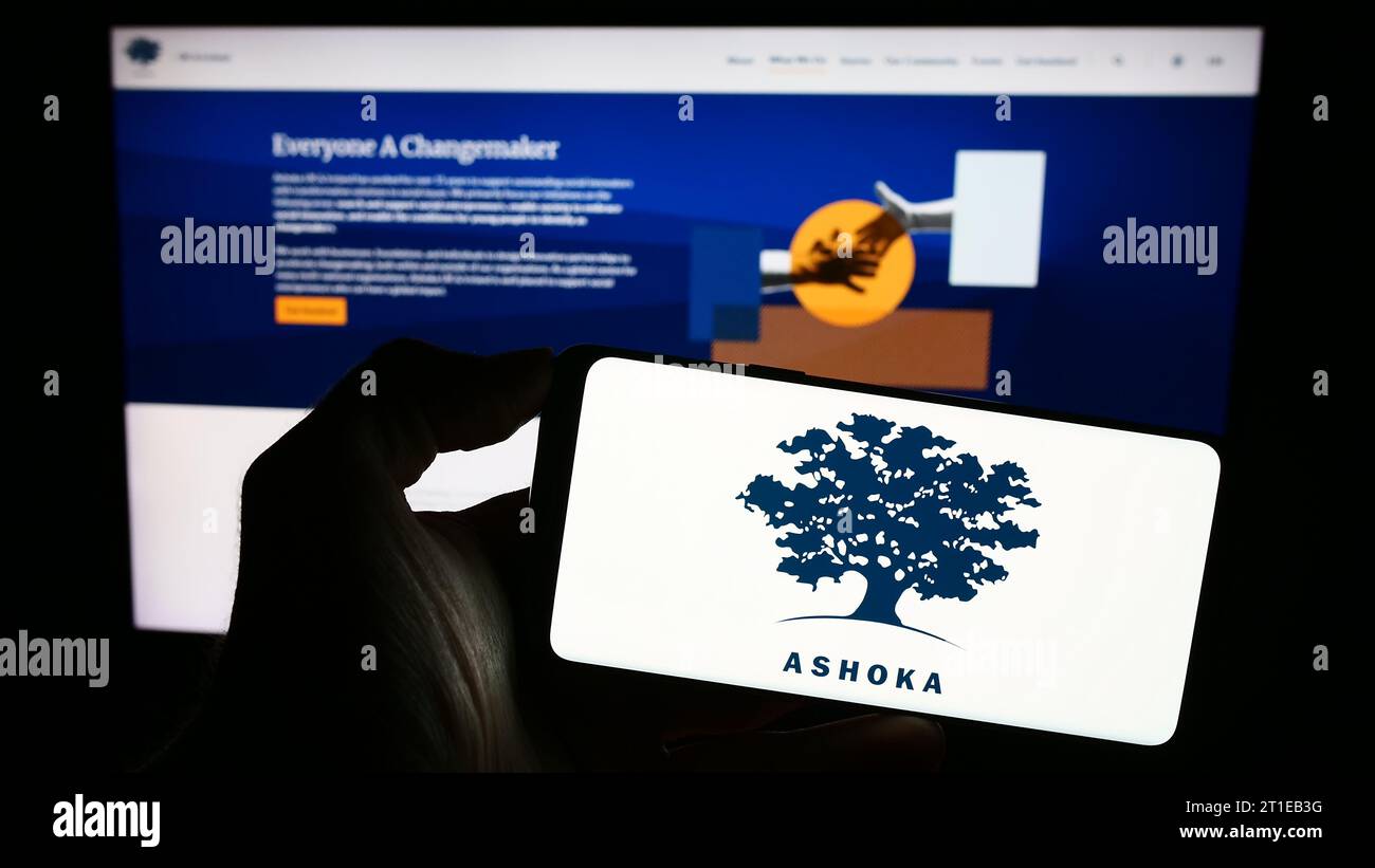 Person holding smartphone with logo of social entrepreneurship organization Ashoka in front of website. Focus on phone display. Stock Photo