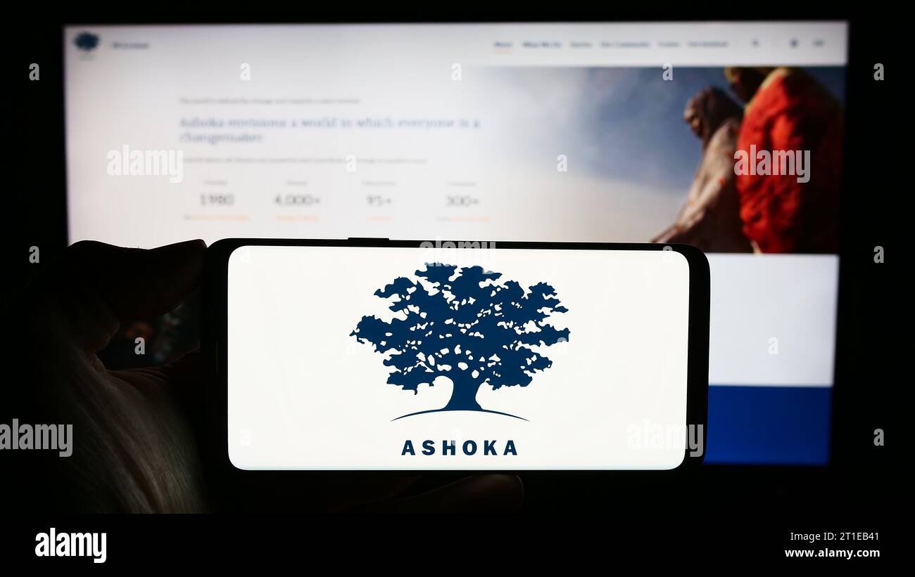 Person holding cellphone with logo of social entrepreneurship organization Ashoka in front of webpage. Focus on phone display. Stock Photo
